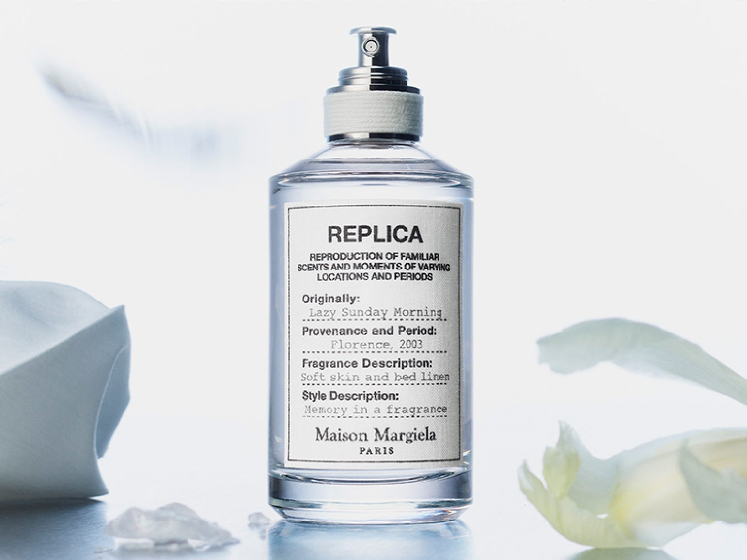 Przezroczysta butelka perfum Replica Lazy Sunday Morning marki Maison Margiela Paris z etykietą opisującą zapach jako miękką skórę i pościel, przywołującą wspomnienia.