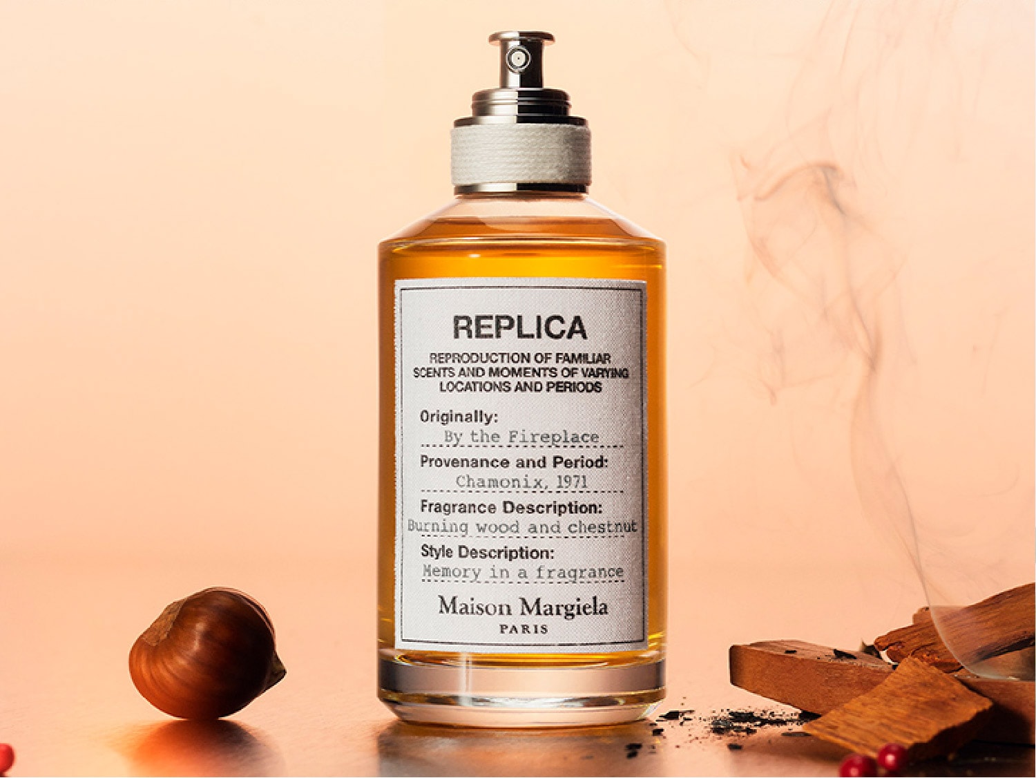 Butelka bursztynowego płynu „Replica By the Fireplace” Maison Margiela Paris, z nutami palonego drewna i kasztanów, przywołuje wspomnienia zapachu.