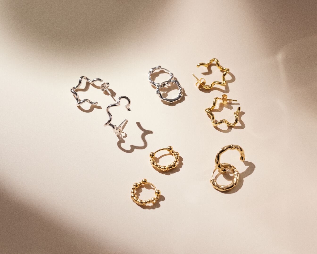 Nahaufnahme von goldenen und silbernen Ohrringen in verschiedenen Designs, die auf einem hellen Hintergrund angeordnet sind.