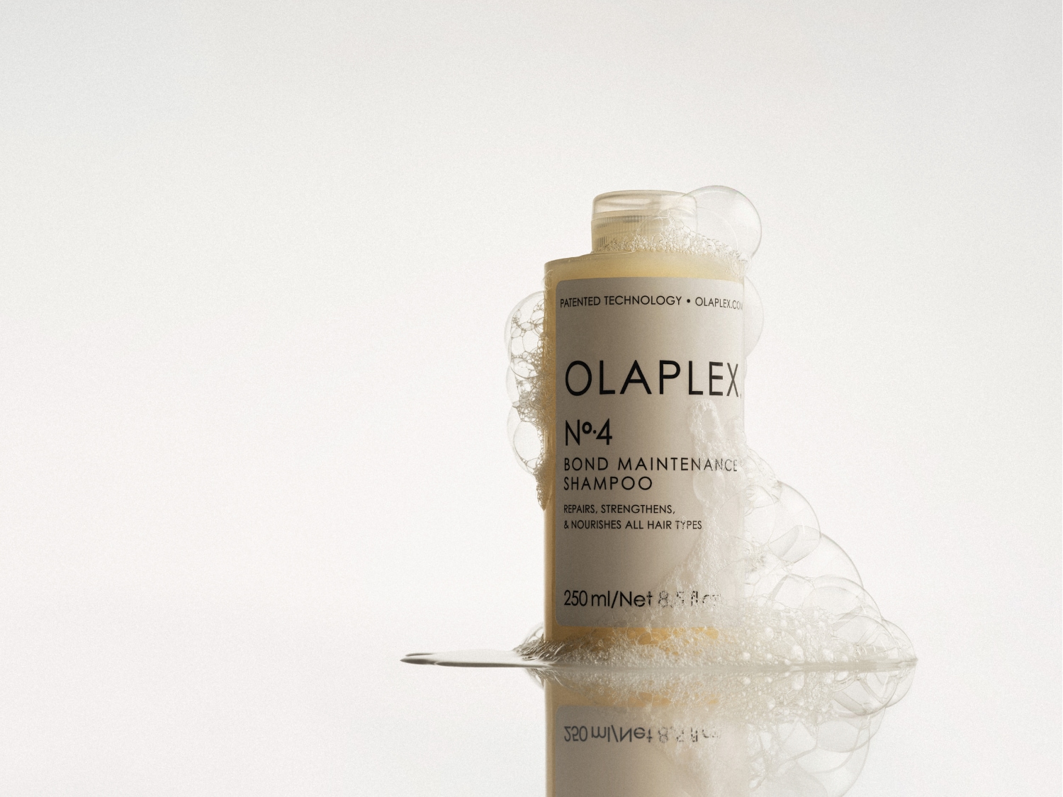 Butelka szamponu Olaplex No.4 Bond Maintenance otoczona pianą, która naprawia, wzmacnia i odżywia wszystkie rodzaje włosów.