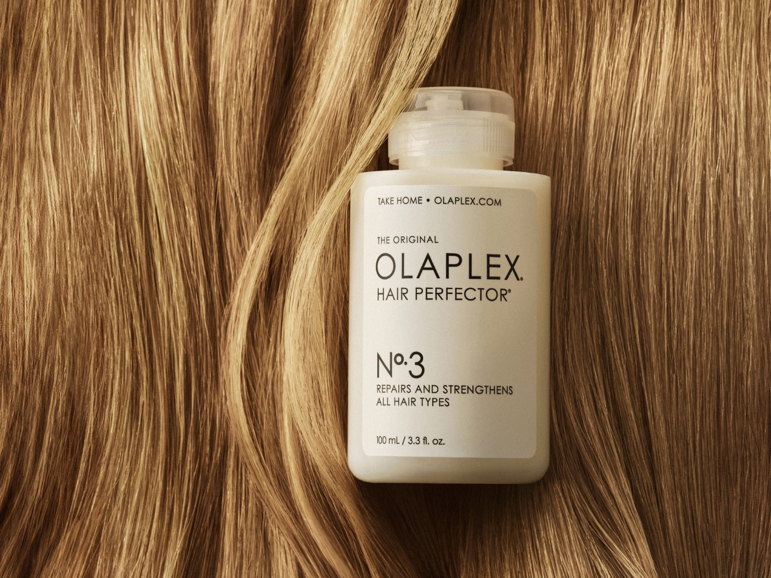 Biała butelka Olaplex Hair Perfector No.3 na tle złotych włosów, obiecująca naprawę i wzmocnienie każdego rodzaju włosów. Sprawdź na Olaplex.com!