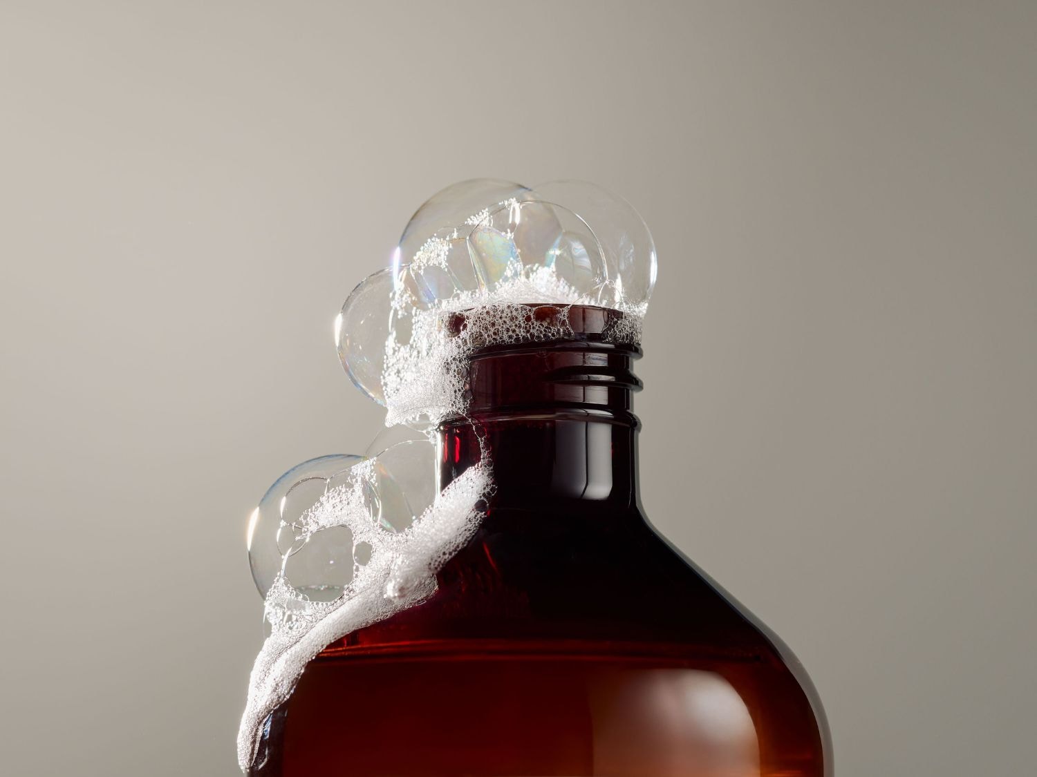 Bruine fles met schuimende zeepbellen die uit de opening komen, tegen een effen achtergrond.