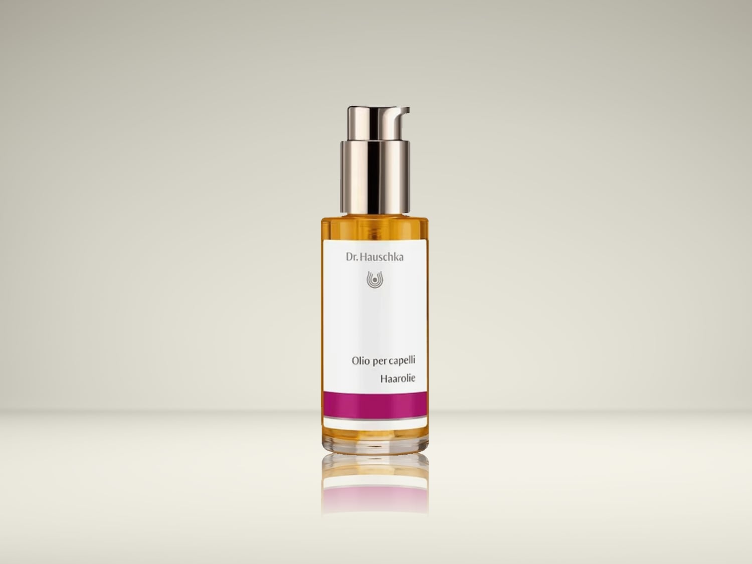Voici l'huile capillaire Dr. Hauschka, présentée dans un flacon transparent avec une pompe argentée, laissant entrevoir une huile dorée, rehaussée d'une étiquette blanche et d'une bande magenta.