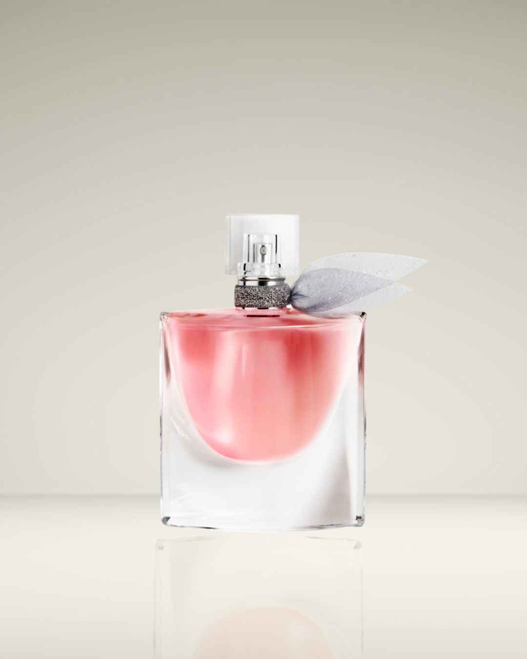 Een heldere glazen parfumfles gevuld met roze vloeistof, afgesloten met een zilveren dop en een doorschijnend grijze strik.