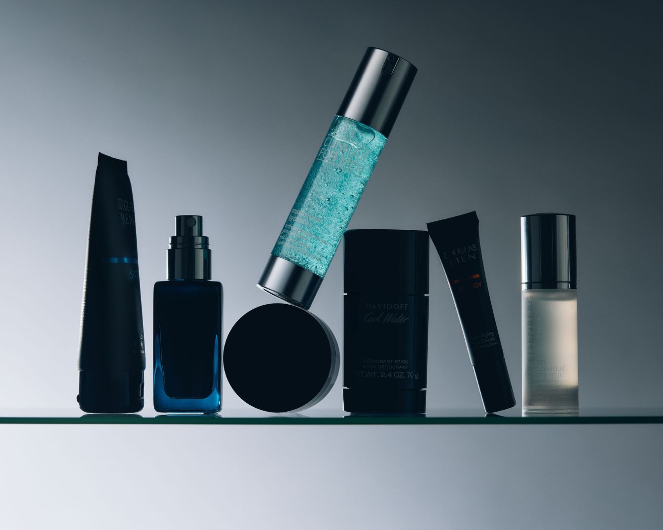 Ontdek een collectie herenverzorgingsproducten, waaronder Douglas Men, Davidoff Cool Water deodorantstick en Eisenberg Gel Contour des Yeux, allemaal gepresenteerd in strakke, donkere verpakkingen.