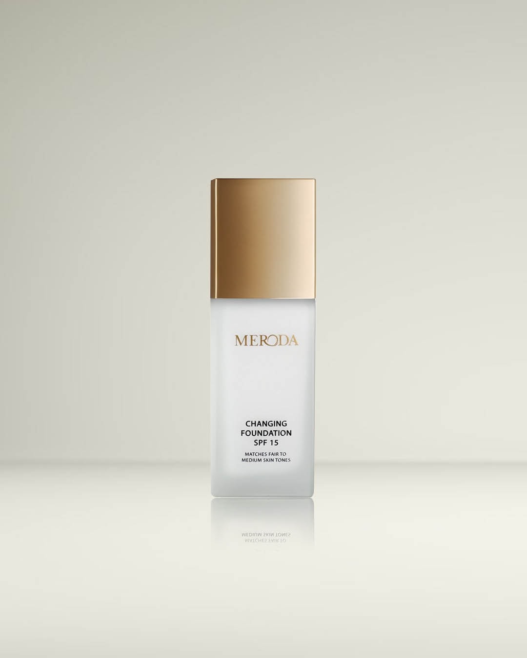 Een matte glazen fles Meroda foundation met een gouden dop, biedt SPF 15 bescherming en is geschikt voor lichte tot medium huidtinten.