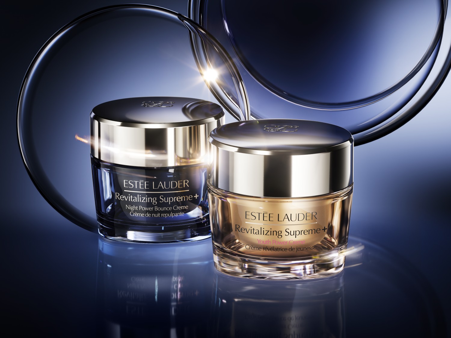 Dwa słoiczki kremu Estée Lauder Revitalizing Supreme+ na ciemnym tle: jeden krem na noc w granatowym opakowaniu, drugi krem na dzień w złotym opakowaniu.