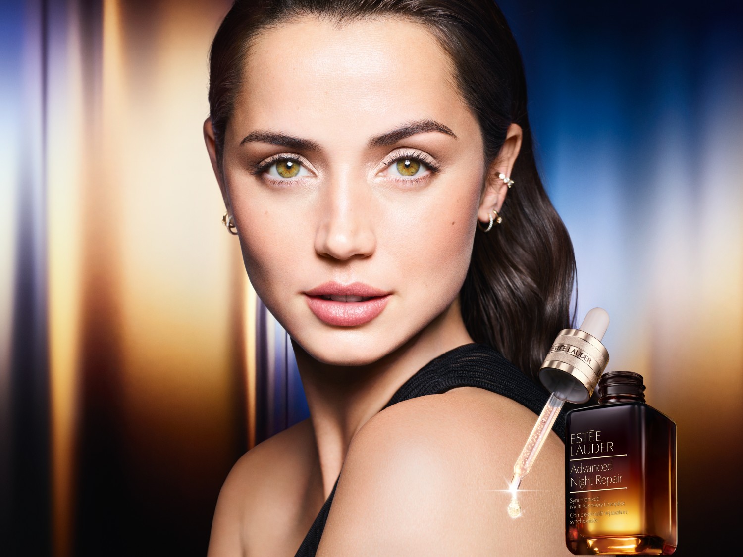 Portret kobiety z serum Estée Lauder Advanced Night Repair; serum ma złotą nakrętkę i pipetę, a płyn wewnątrz jest lekko opalizujący, co sugeruje jego nawilżające i regenerujące właściwości.