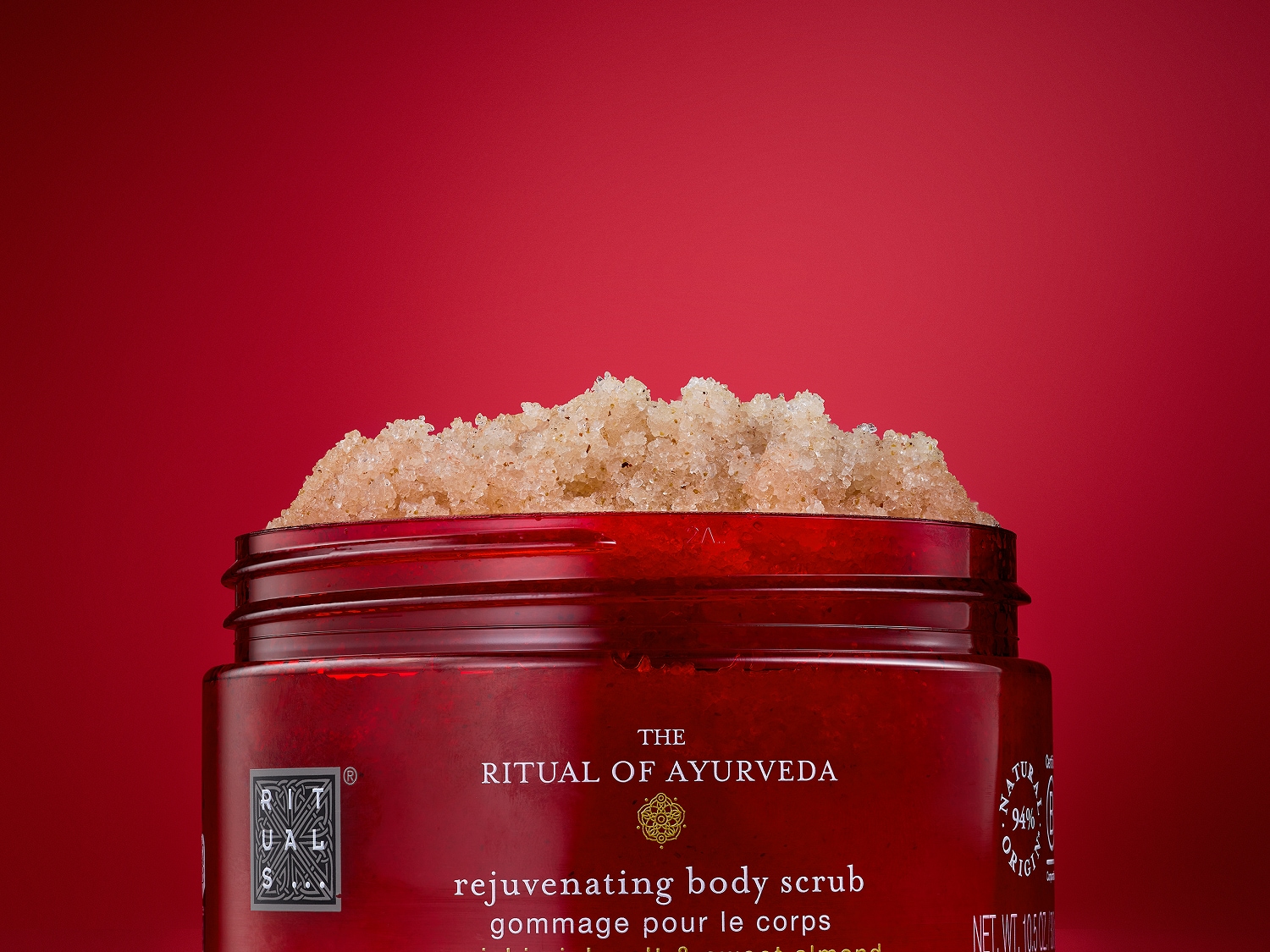 Czerwony słoik z peelingiem do ciała Ritual of Ayurveda z kryształkami soli i słodkich migdałów, zapewniający efekt odmłodzenia.