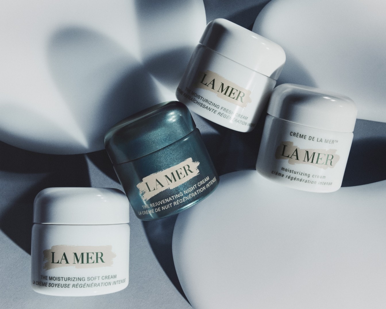 Cztery kremy La Mer w białych i turkusowych opakowaniach, w tym The Moisturizing Fresh Cream i The Rejuvenating Night Cream, obiecują intensywne nawilżenie i regenerację.
