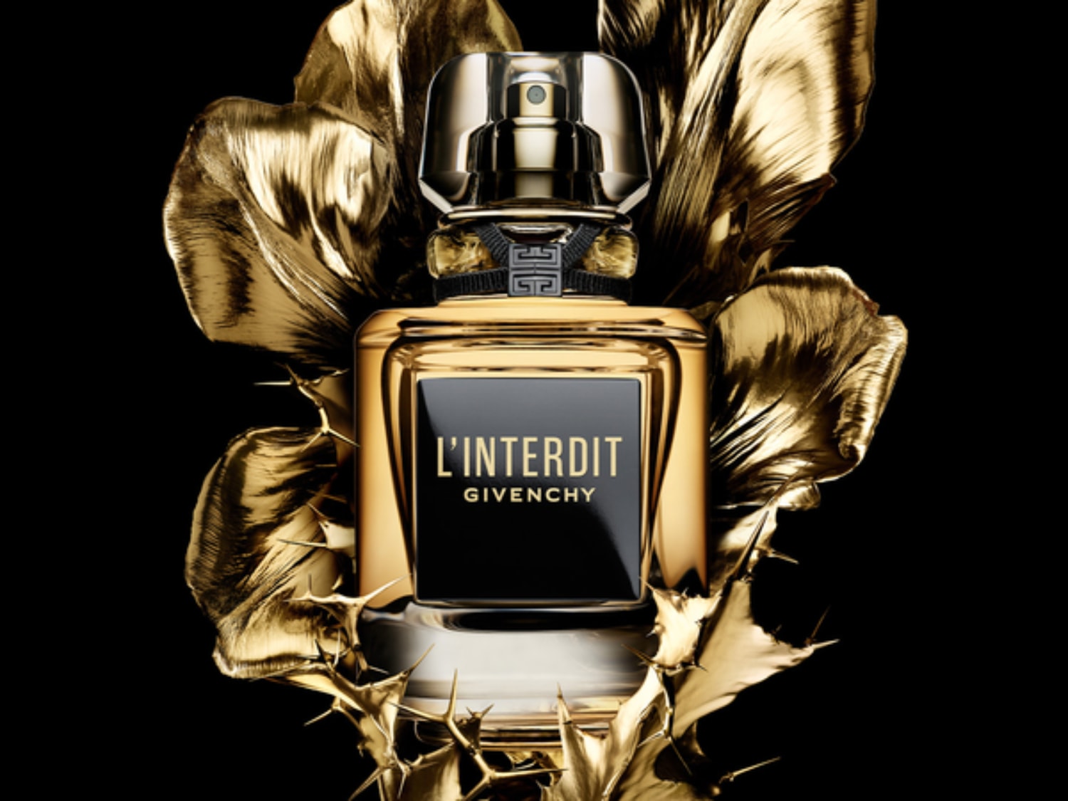 Gouden L'Interdit Givenchy parfumflesje met zwarte details, omringd door gouden bladeren tegen een zwarte achtergrond.