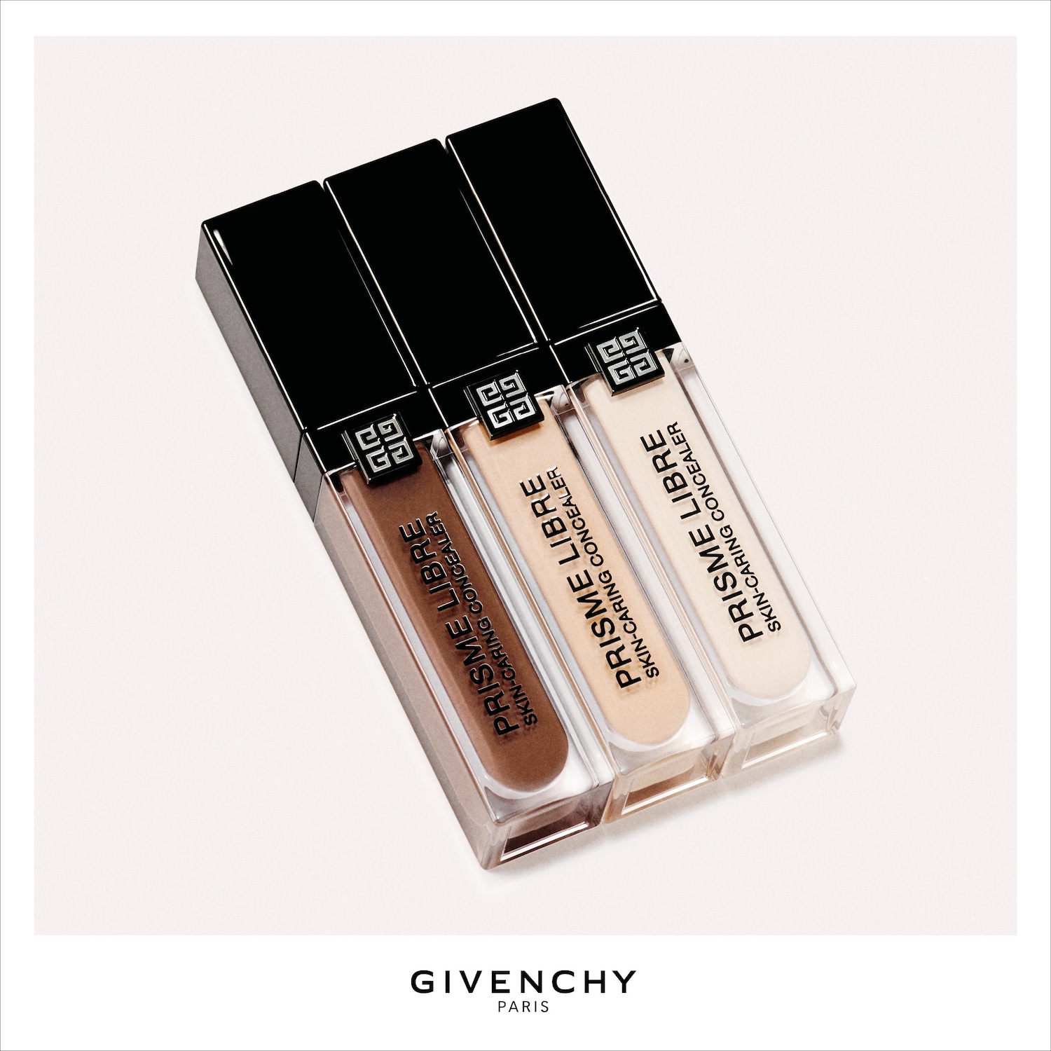 Drie Givenchy Prisme Libre Skin-Caring Concealers in verschillende huidtinten, variërend van licht tot donkerbruin, staan rechtop met zwarte doppen en het Givenchy-logo, klaar om de huid te perfectioneren.