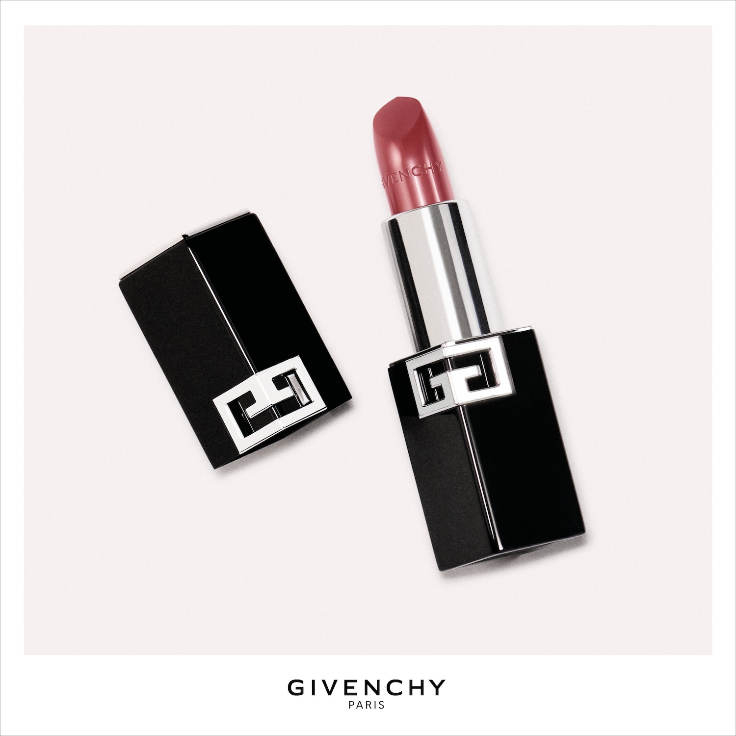 Een open Givenchy Le Rouge Interdit Intense Silk lipstick in een zwarte huls met zilveren accenten, toont een roze-rode kleur met de merknaam op de lipstick.