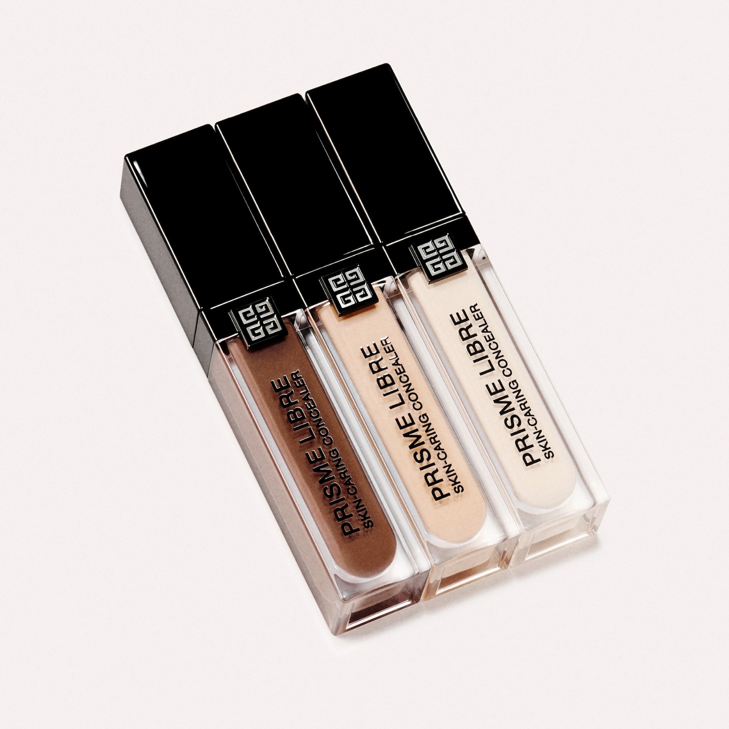 Drie Givenchy Prisme Libre Skin-Caring Concealers in bruin, beige en ivoor, elk in een transparante verpakking met een zwarte dop.