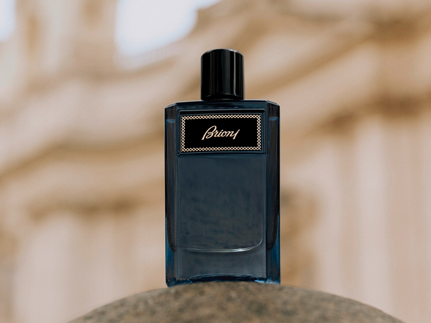 Butelka ciemnoniebieskich perfum Brioni z czarną zakrętką i złotym napisem na etykiecie, stojąca na kamiennej powierzchni.