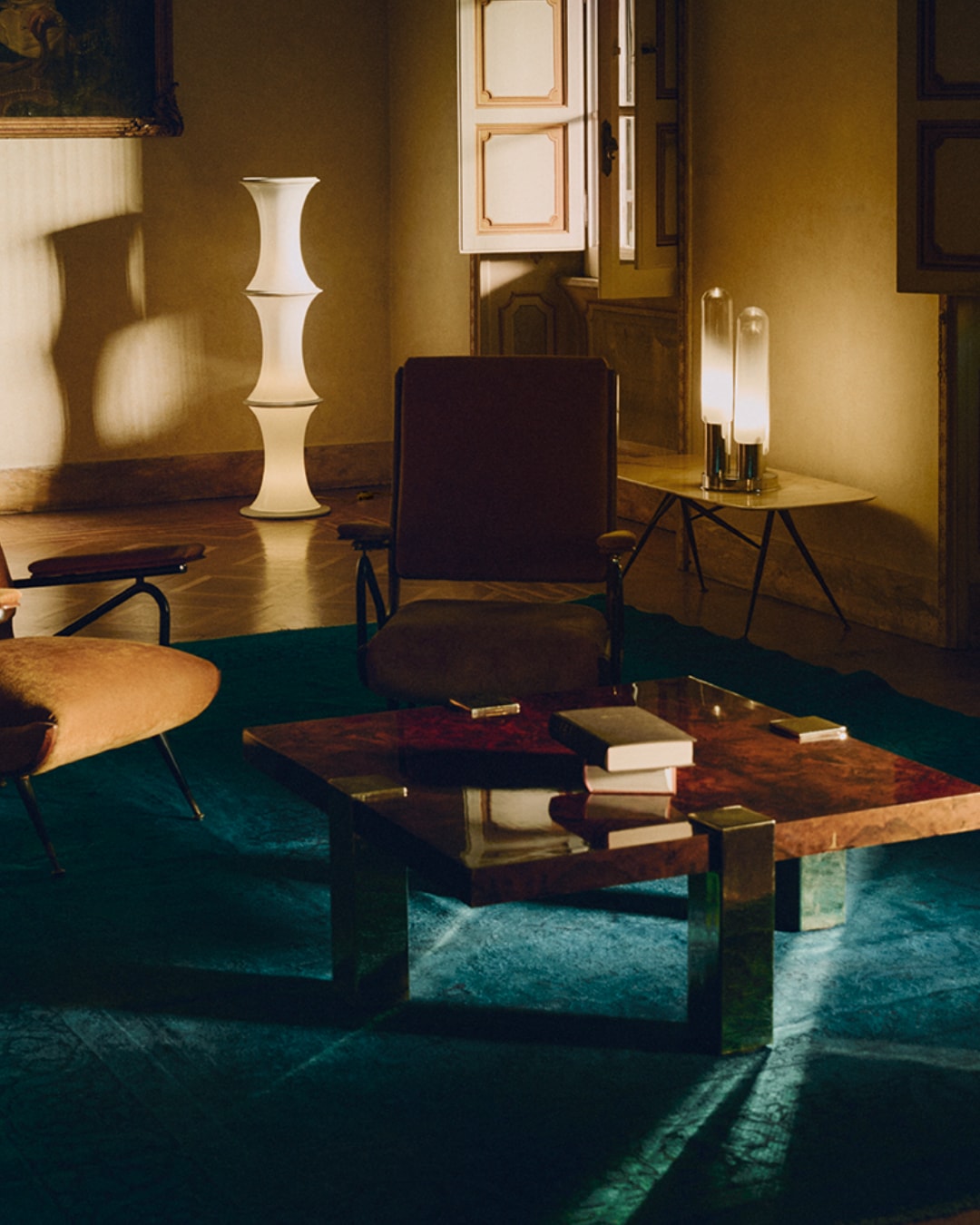 Wnętrze pokoju z brązowym fotelem, stolikiem kawowym z książkami i lampami, oświetlone ciepłym światłem, tworzące przytulną atmosferę.