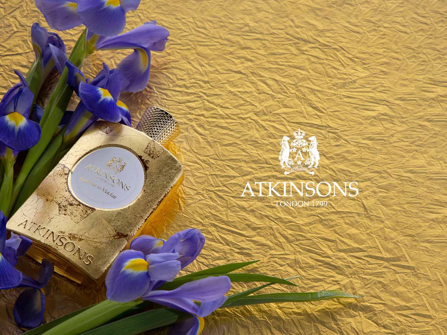 Złota butelka perfum Atkinsons Covent Garden in Mayfair otoczona fioletowymi kwiatami na złotym tle.