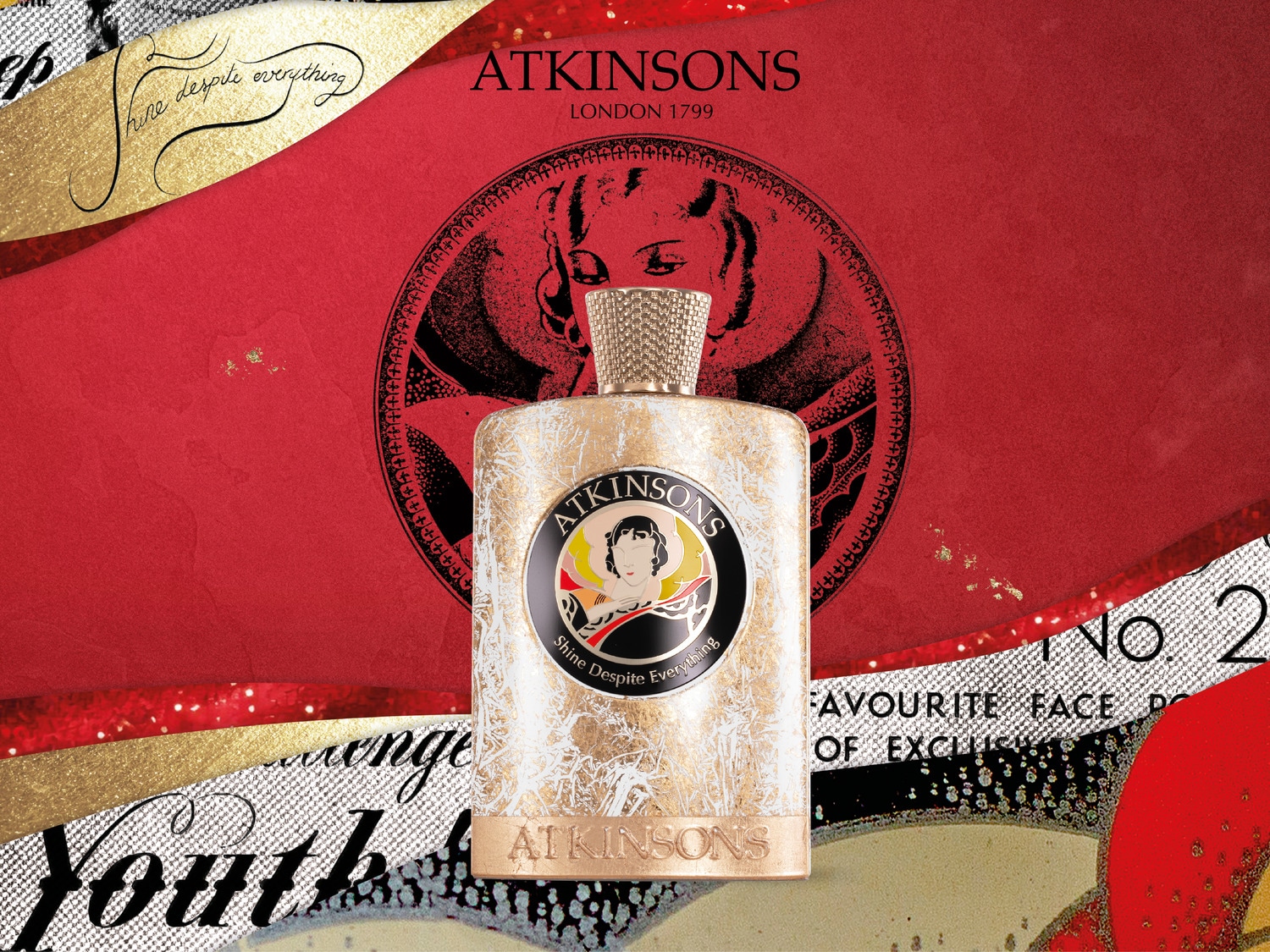Perfumy Atkinsons w ozdobnym, złotym flakonie z napisem "Shine Despite Everything" na tle czerwono-złotego wzoru z hasłem "Shine Despite Everything".