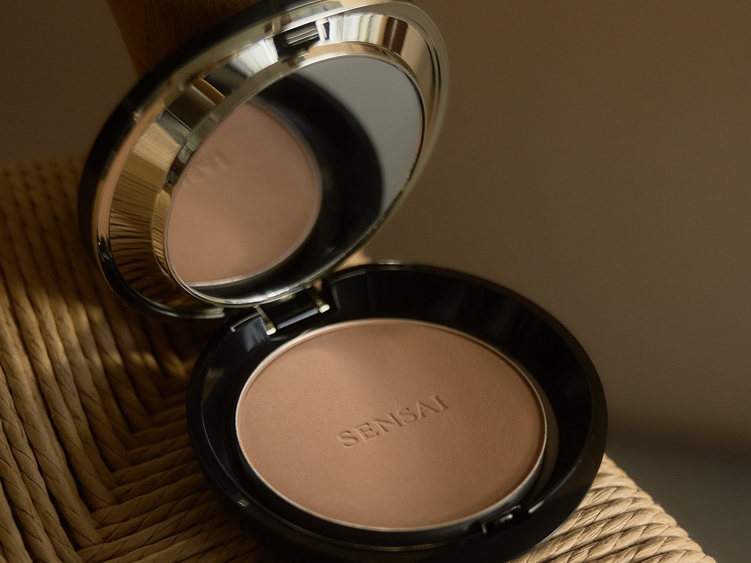Puder Sensai w czarnym opakowaniu z lusterkiem, otwarty, ukazujący prasowany puder o odcieniu skóry.