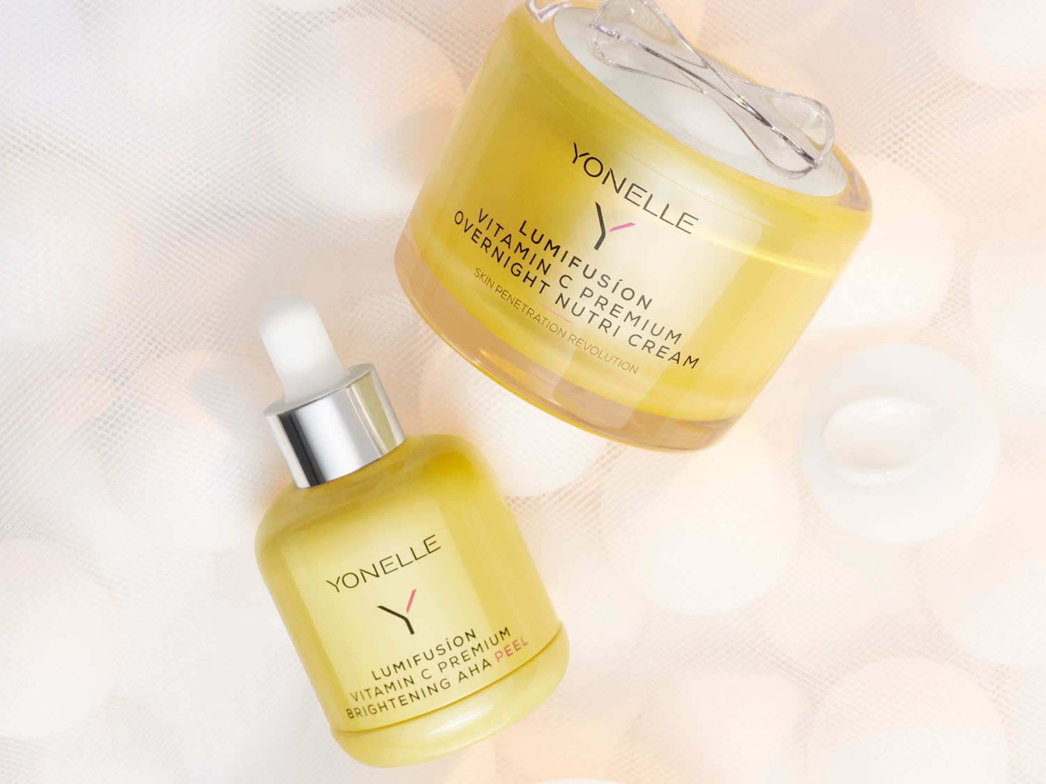 A Yonelle Lumifusion Vitamin C Premium termékcsaládjának termékei láthatók: egy tégelyes éjszakai krém és egy AHA hámlasztó, mindkettő világos sárga színű.