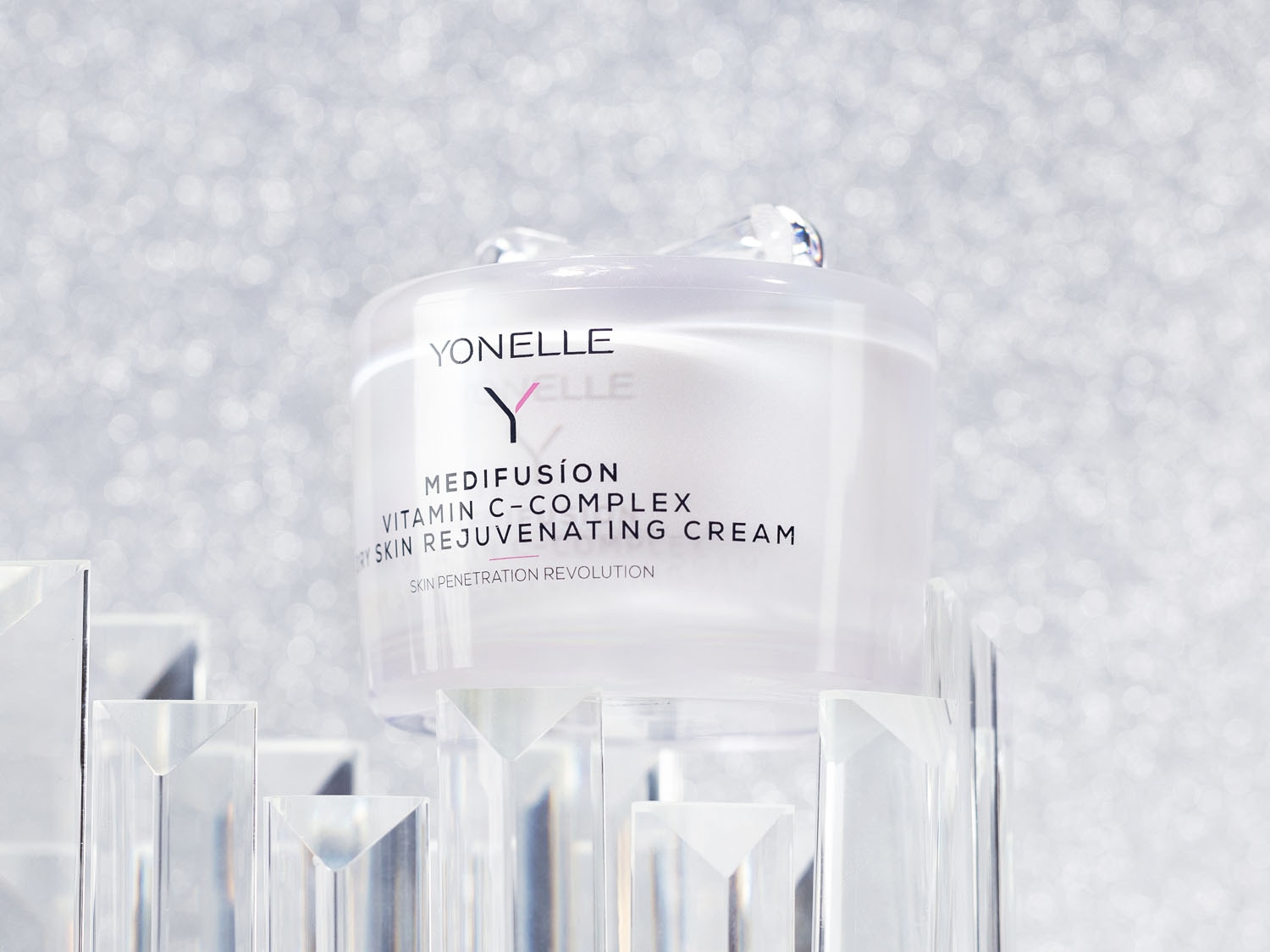 A Yonelle Medifusión Vitamin C-Complex bőrfiatalító krém áttetsző tégelyben, ezüstösen csillogó háttér előtt, akril lépcsőn áll.