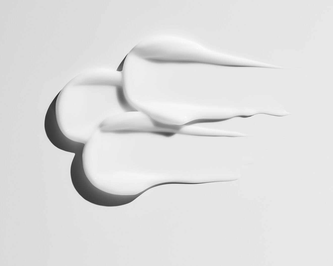 Nahaufnahme von weißen, cremigen Hautpflegeprodukten, die in sanften, geschwungenen Linien aufgetragen wurden.