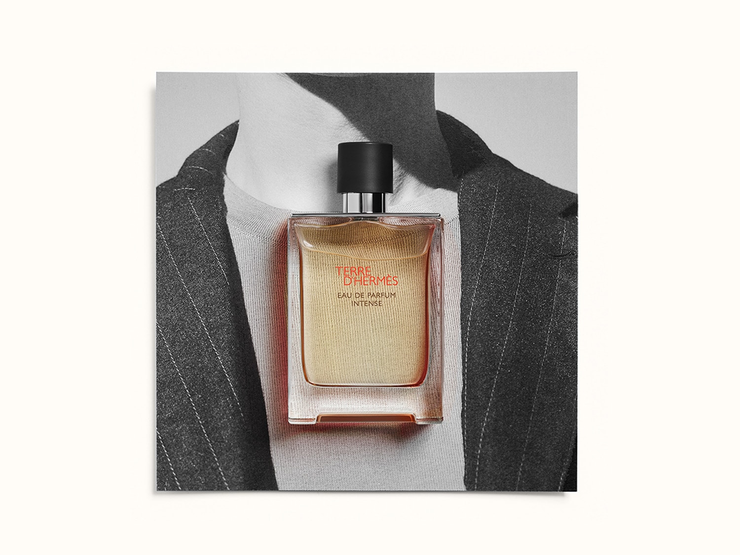 Een flacon Terre d'Hermès Eau de Parfum Intense staat voor een zwart-wit foto van een man in pak, de geur zelf is amberkleurig en straalt warmte uit.