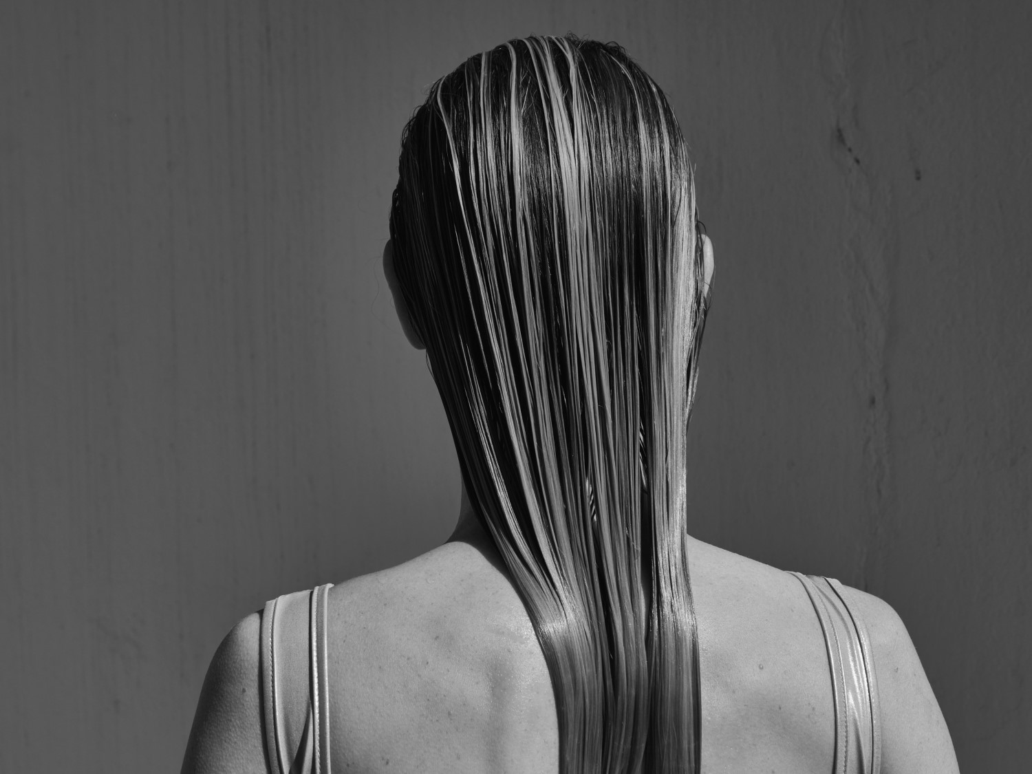 Schwarz-Weiß-Aufnahme einer Frau mit glattem, nassem Haar, das ihren Rücken hinunterfließt, was die Textur und den Glanz des Haares hervorhebt.