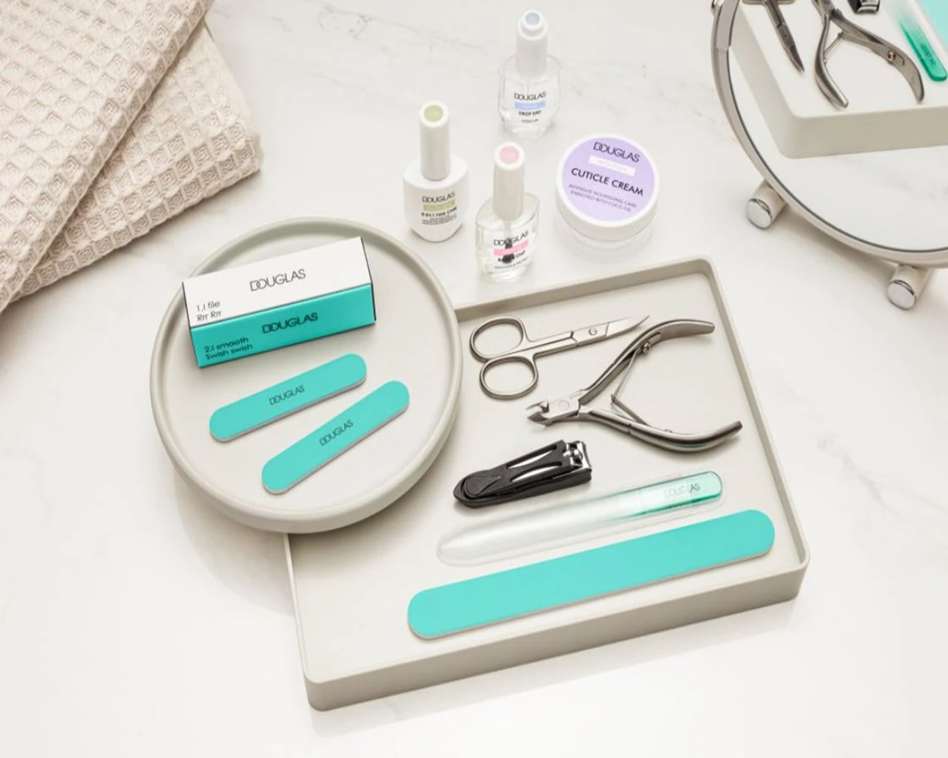 Das Bild zeigt eine Auswahl an Maniküreprodukten von Douglas, darunter Nagellacke, Nagelfeilen, eine Dose mit Nagelcreme und verschiedene Werkzeuge für die Nagelpflege, die auf einem Tablett angeordnet sind.