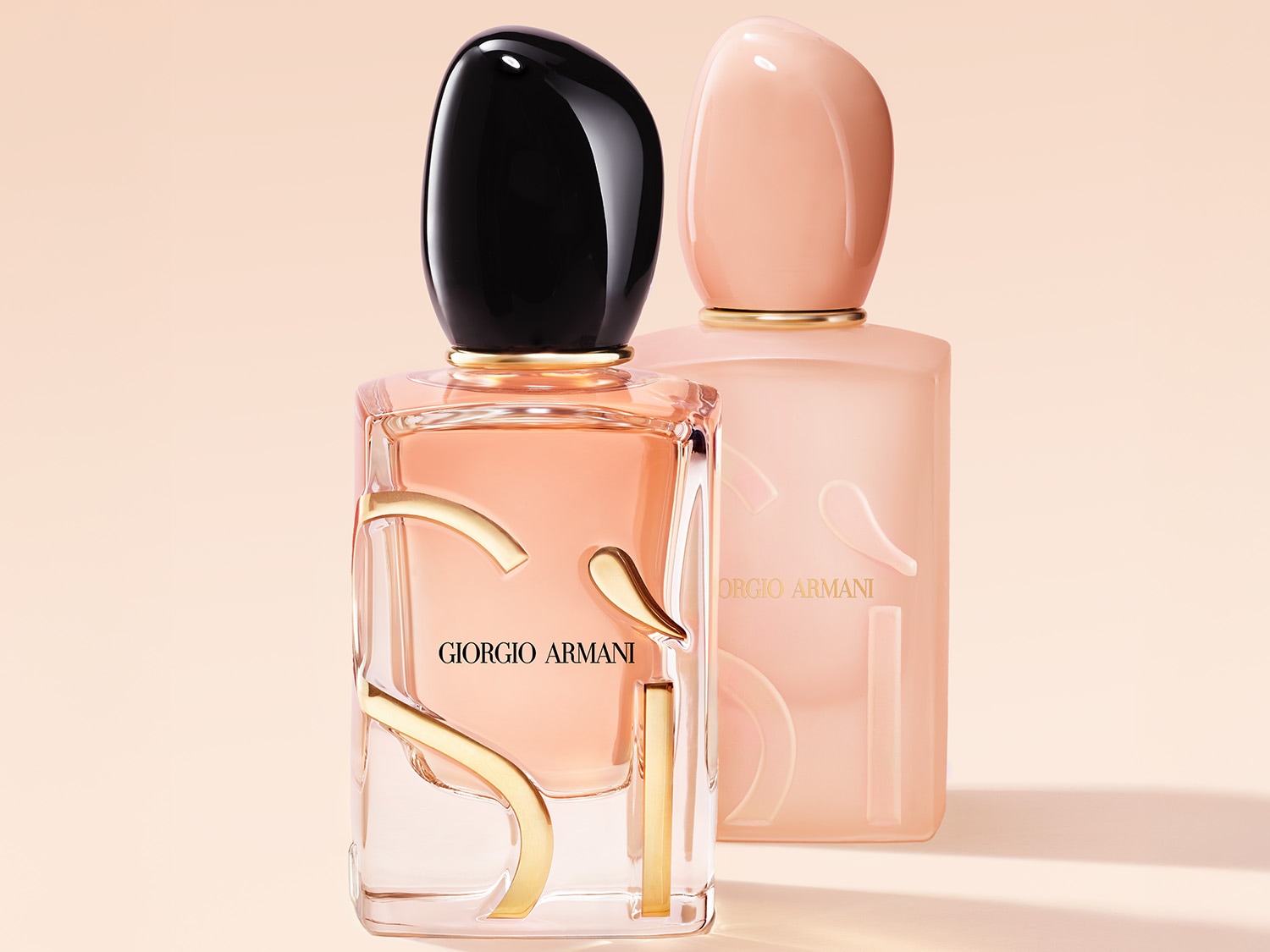 Dwa flakony perfum Giorgio Armani Si, jeden przezroczysty z różowym płynem i czarną nakrętką, a drugi matowy, różowy z różową nakrętką, stoją obok siebie na jasnym tle.