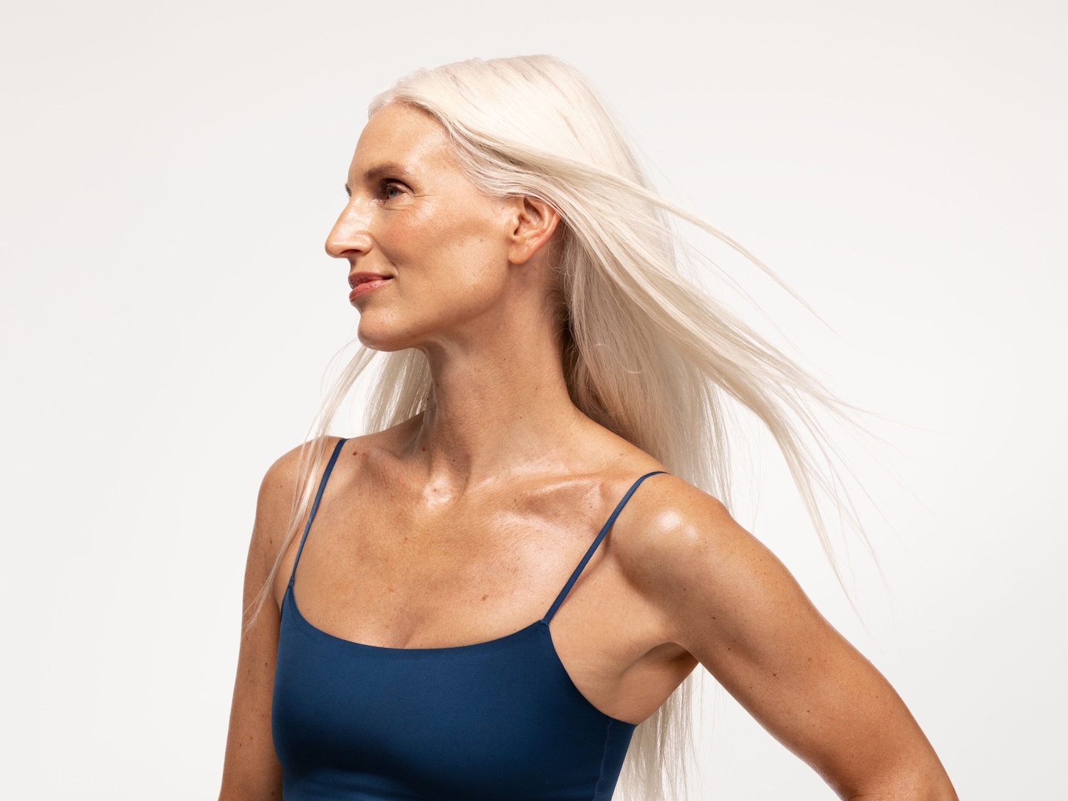 Profilansicht einer Frau mit langen, weißen Haaren und einem blauen Top, die anmutig zur Seite blickt.