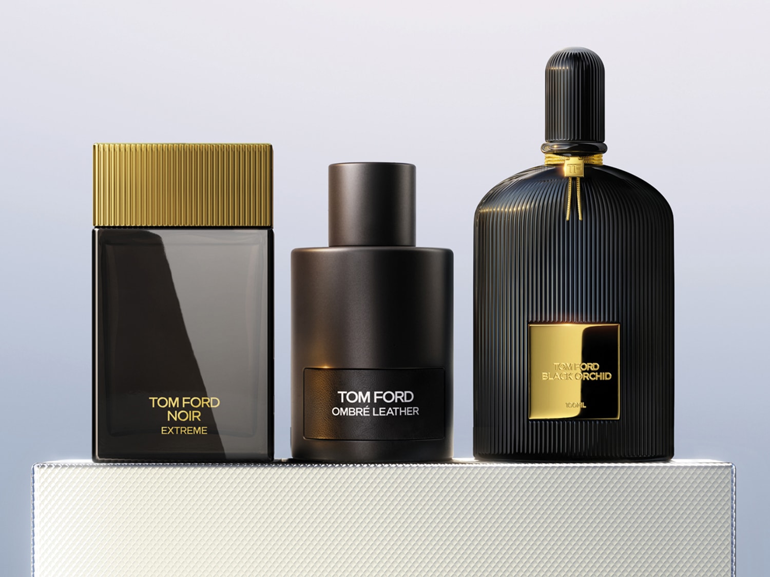 Tre flaconi di profumo Tom Ford: Noir Extreme con tappo dorato, Ombre Leather e Black Orchid con dettagli dorati, presentati su una base elegante.