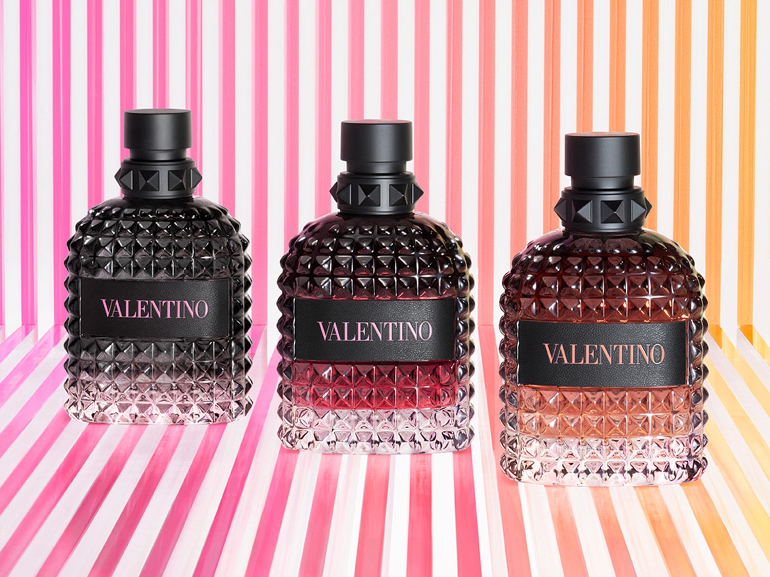 Trzy flakony perfum Valentino w odcieniach czerni, czerwieni i brązu, każdy z czarnym korkiem i nazwą marki na etykiecie.