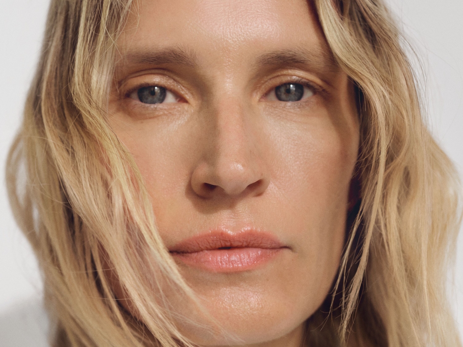 Nahaufnahme einer Frau mit blonden Haaren, blauen Augen und einem natürlichen Make-up-Look, der ihre Gesichtszüge hervorhebt.