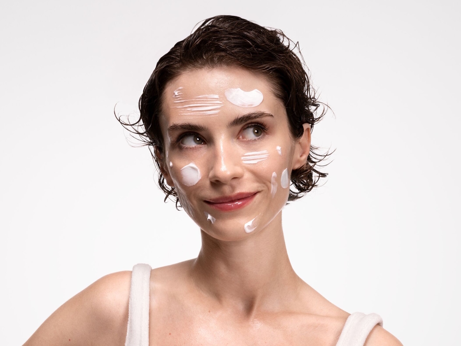 Nahaufnahme einer Frau mit kurzen, dunklen, nassen Haaren und weißer Creme auf Gesicht und Stirn, die nach links oben schaut.