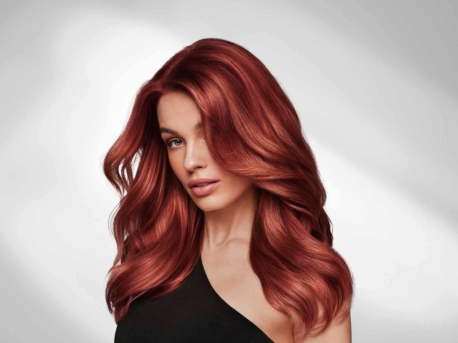 Eine Frau mit langen, gewellten, rotbraunen Haaren blickt in die Kamera, ihr Haar glänzt und fällt sanft über ihre Schulter.