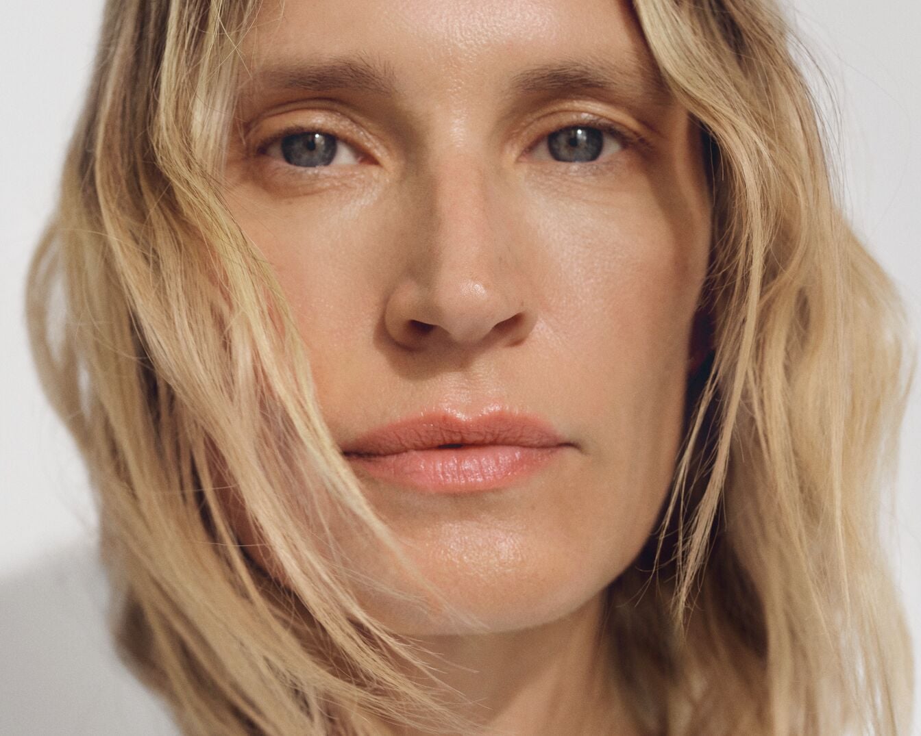 Nahaufnahme einer Frau mit blonden, gewellten Haaren, hellen Augen und einem natürlichen Make-up, das ihre Gesichtszüge betont.