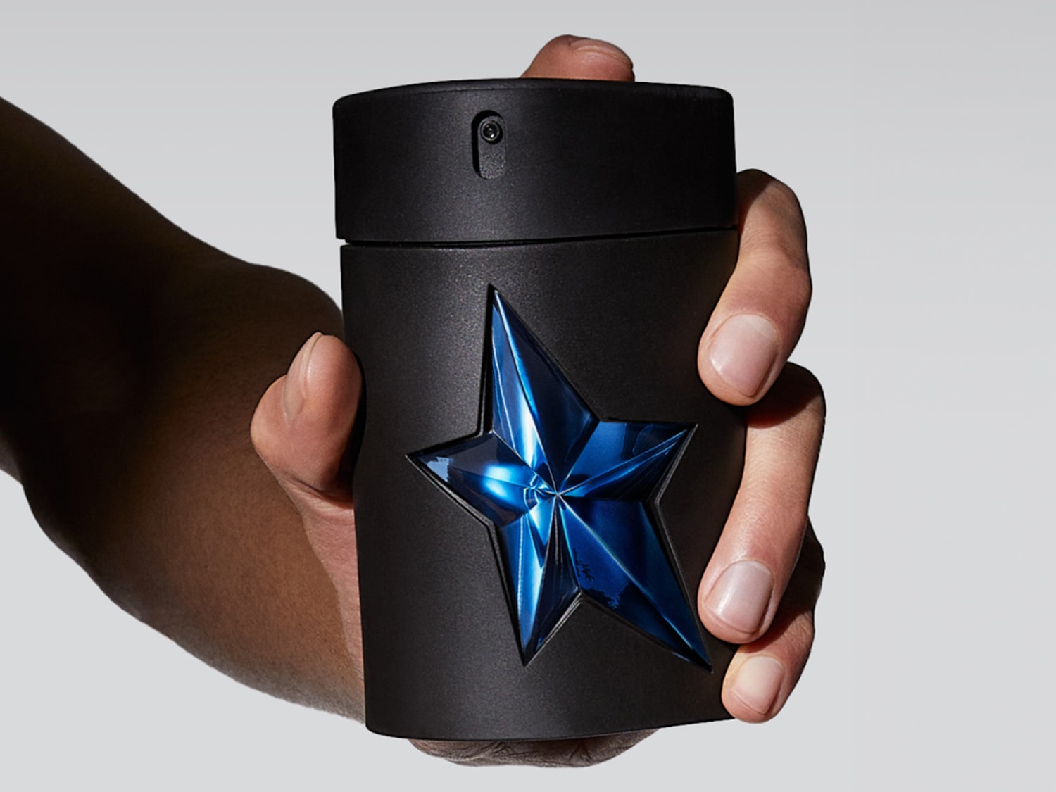 Gros plan sur un flacon de parfum noir mat, orné d'une étoile bleue brillante, tenu délicatement dans une main, évoquant un parfum masculin et sophistiqué.