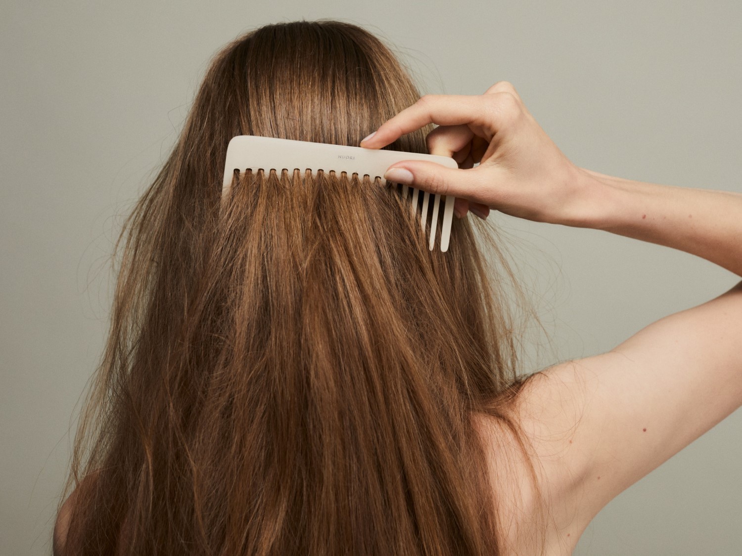 Eine Person kämmt ihr langes, braunes Haar mit einem hellen Kamm, um es zu entwirren und zu glätten.