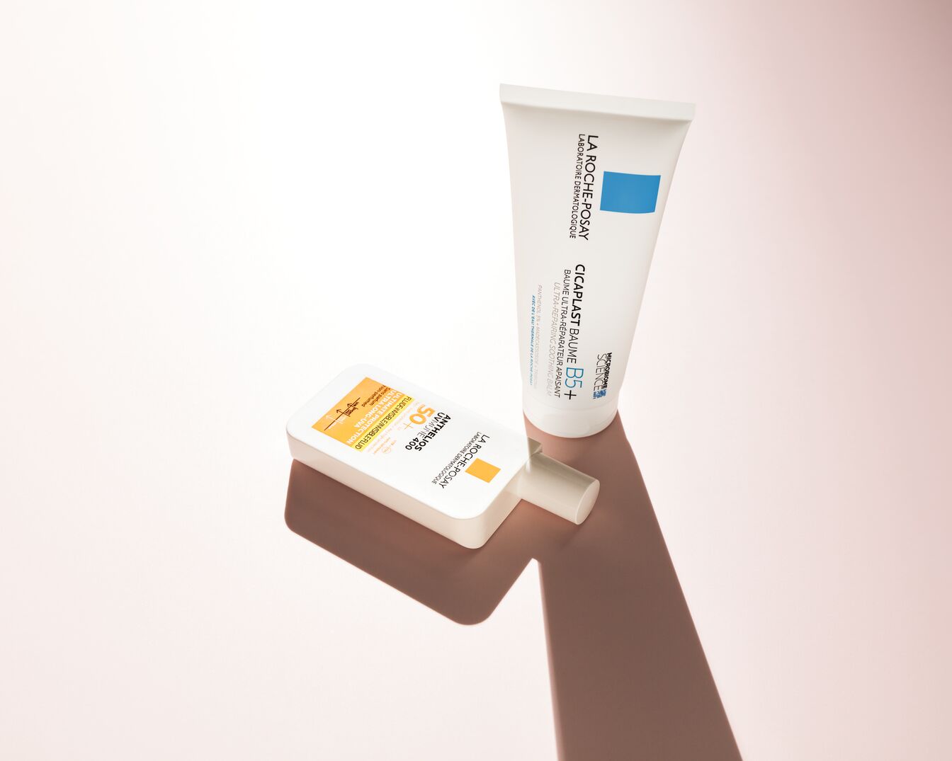 Zu sehen sind der Sonnenschutz Anthelios UVMUNE 400 SPF 50+ von La Roche-Posay in einer weißen Flasche mit orangefarbenem Etikett und der reparierende und beruhigende Balsam Balsam Cicaplast Baume B5+ in einer weißen Tube mit blauem Etikett.