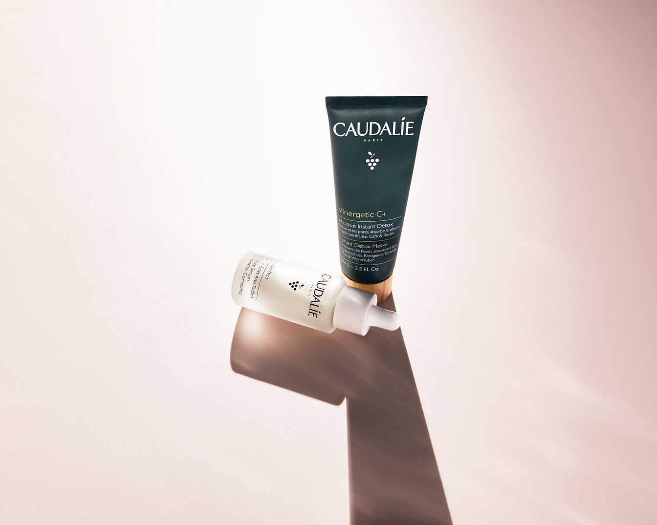 Das Bild zeigt zwei Hautpflegeprodukte von Caudalie: eine grüne Tube Vinergetic C+ Instant Detox Maske und eine weiße Flasche Vinoperfect Serum, die für einen strahlenden Teint und zur Korrektur von Pigmentflecken sorgen.