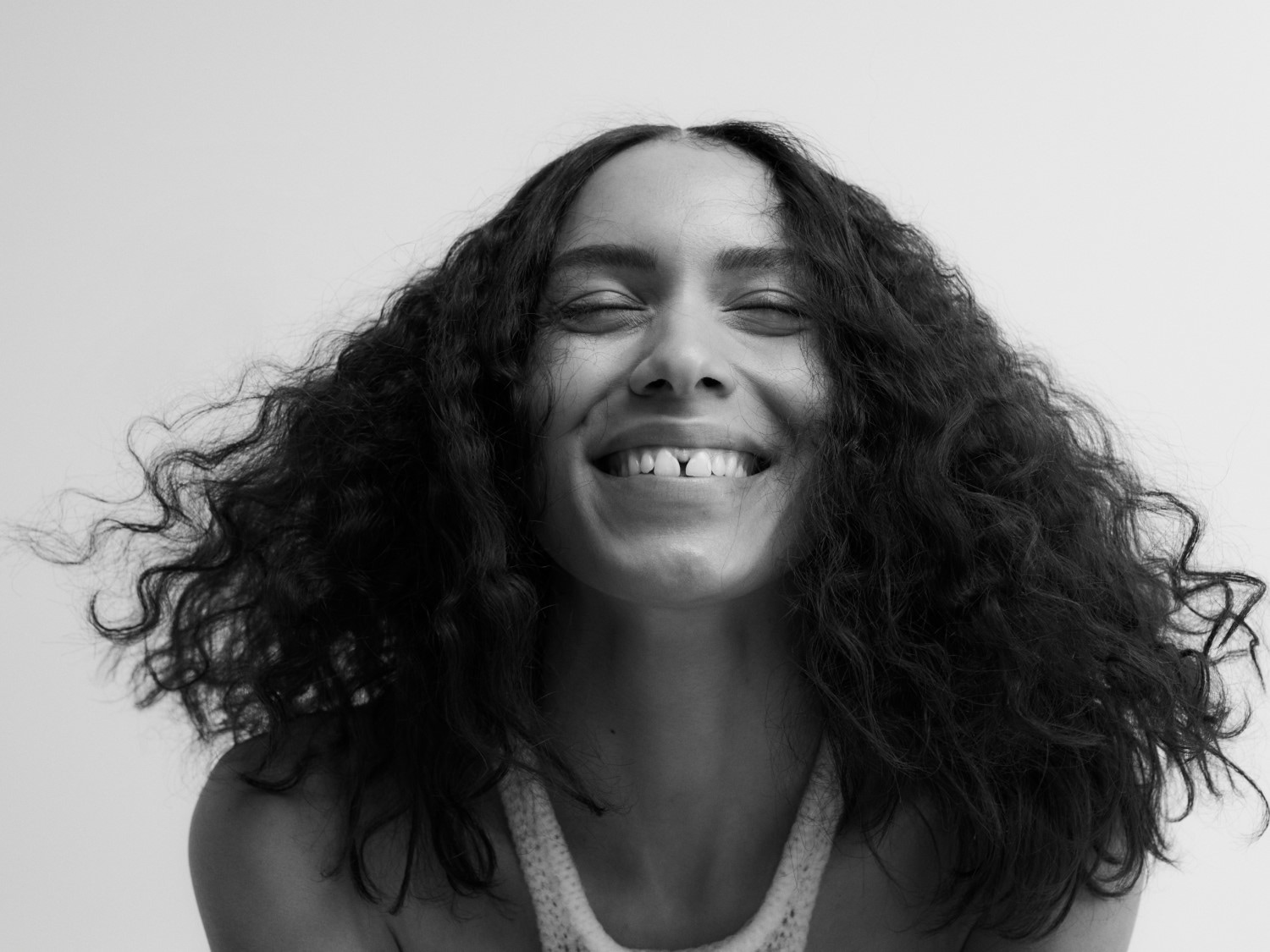 Portrait en noir et blanc d'une femme souriante aux cheveux bouclés et aux yeux fermés, exprimant la joie et la positivité.