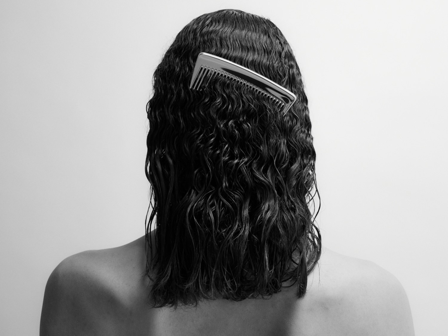 Rückansicht einer Person mit nassem, gewelltem Haar und einem silbernen Kamm, der im Haar steckt.
