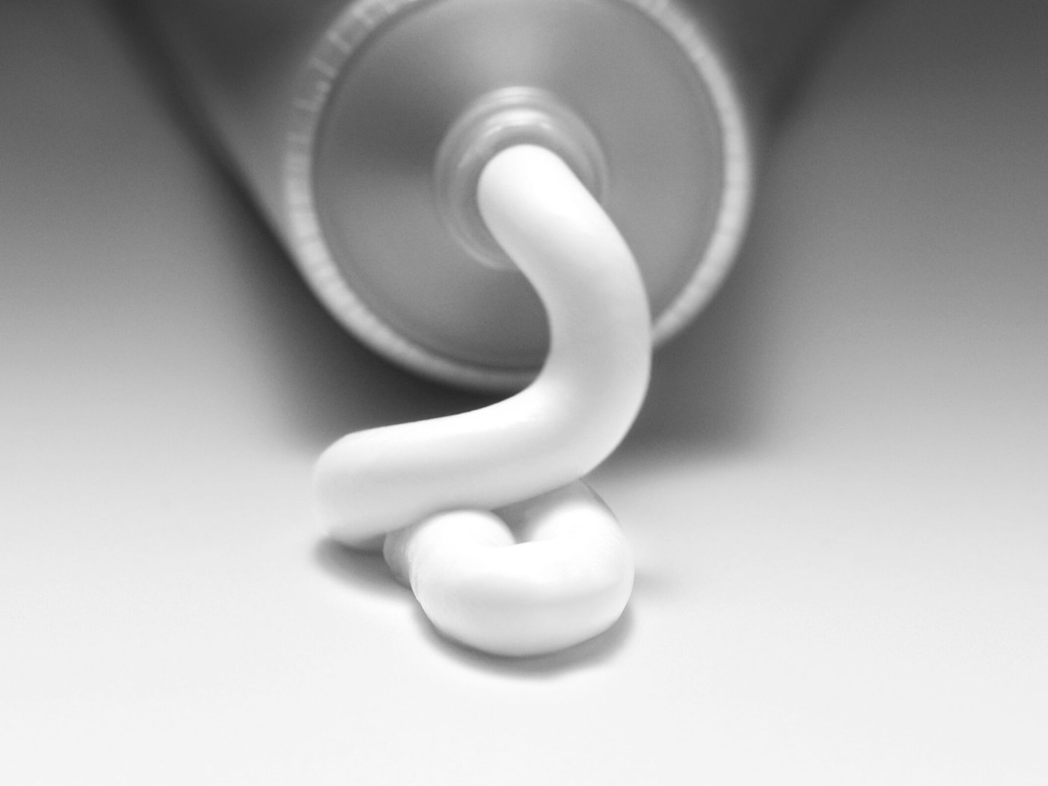 Primer plano de un tubo de metal con una espiral de crema blanca saliendo, mostrando la textura suave y brillante del producto.