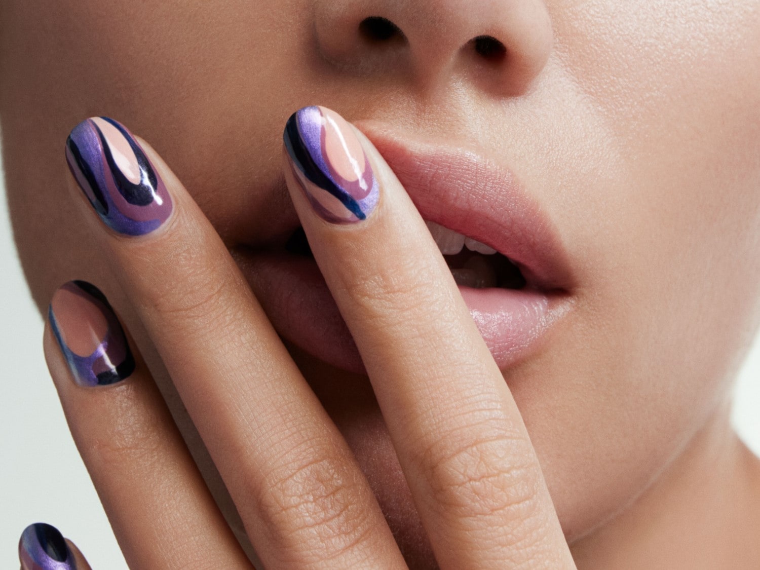 Nahaufnahme einer Frau, deren Finger mit einem abstrakten, lila-farbenen Nageldesign ihre Lippen berühren.