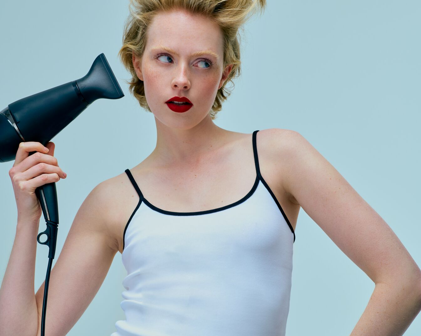 Blonde Frau mit roten Lippen hält einen schwarzen Föhn in der Hand, um ihr Haar zu stylen.