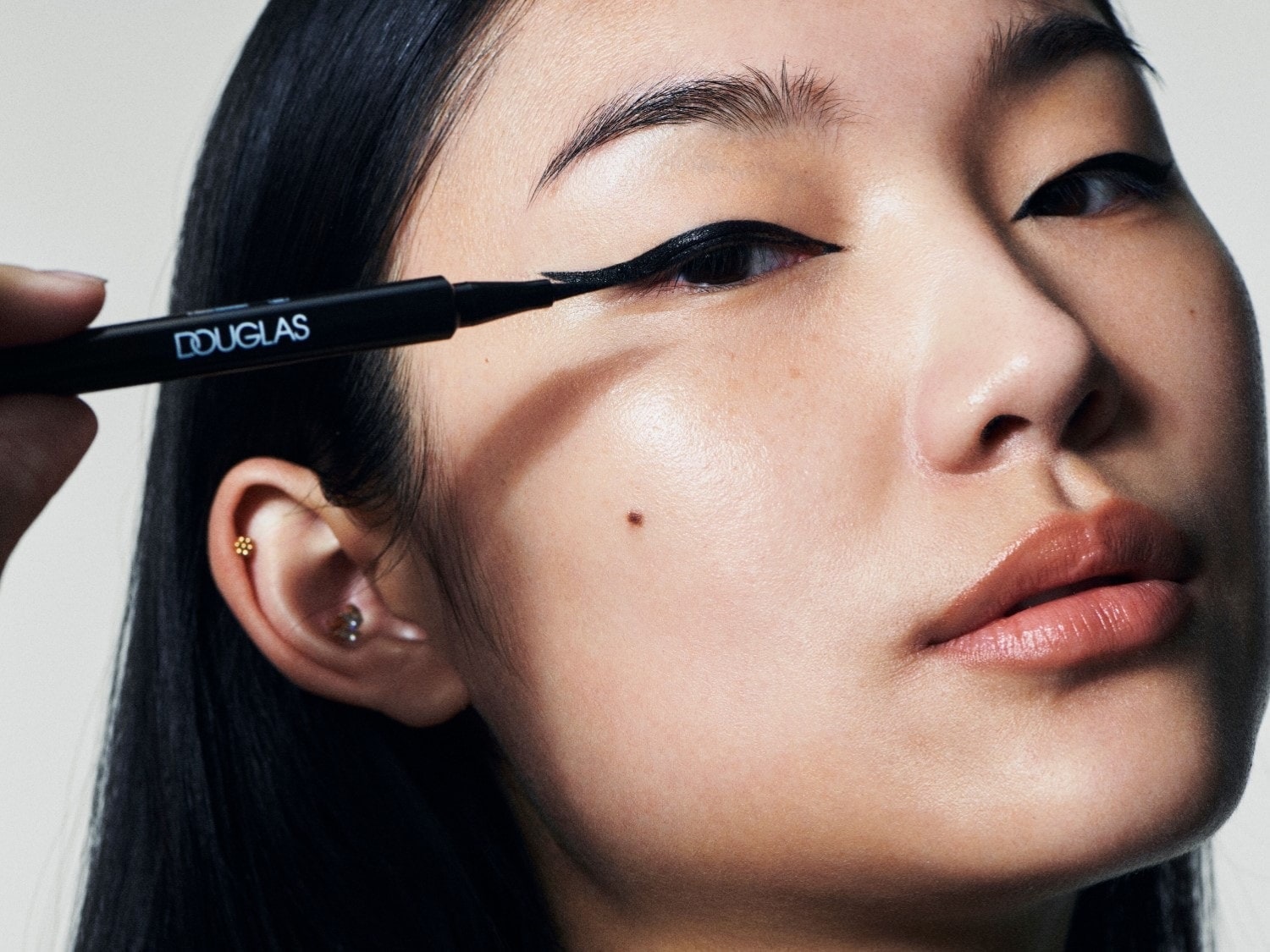 Primo piano di una donna che applica l'eyeliner nero Douglas per un look occhi definito e intenso.