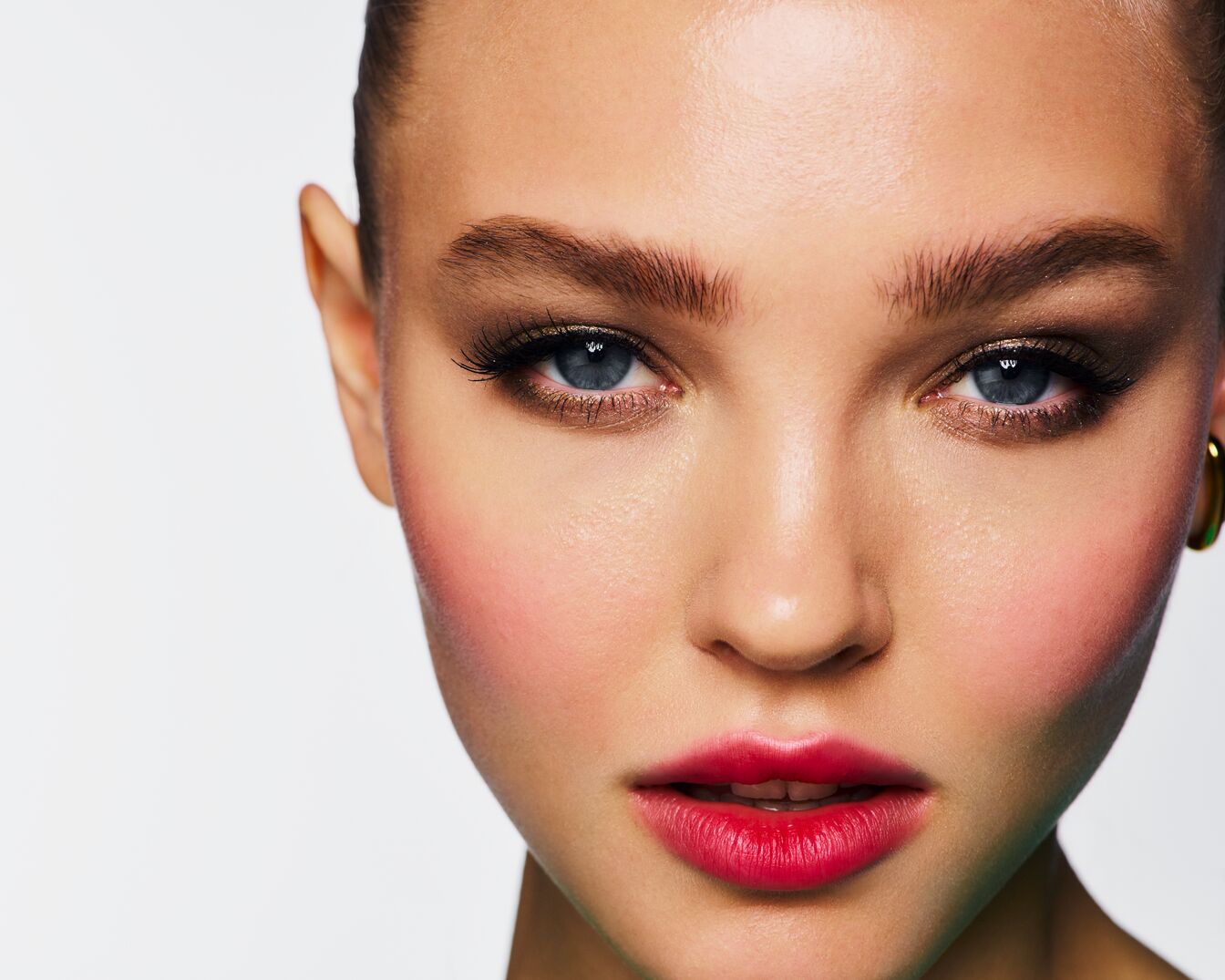 Nahaufnahme eines Frauengesichts mit strahlend blauen Augen, betont durch dunklen Lidschatten und lange Wimpern, dazu rosige Wangen und leuchtend rote Lippen.