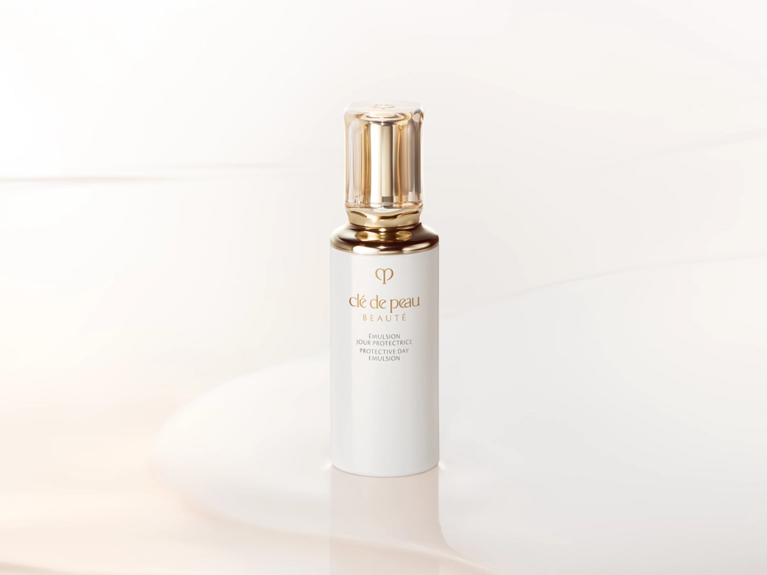 Voici l'émulsion protectrice de jour Clé de Peau Beauté dans un flacon blanc élégant avec un bouchon doré.