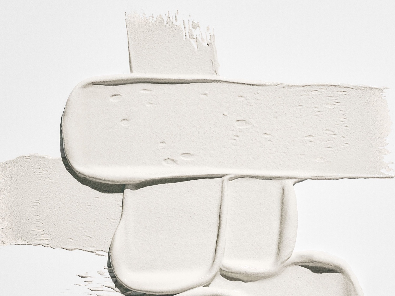 Nahaufnahme von weißen Creme- oder Maskenabstrichen, die eine dicke, glatte Textur auf einer ebenen Fläche zeigen.